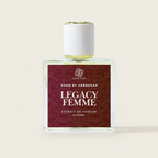 Perfume bottle labeled 'Legacy Femme' by Osho by Abroshah on a table with plants in the background